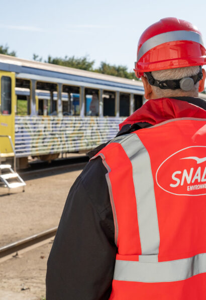 Technicien SNADEC avec casque rouge et gilet haute visibilité sur un site ferroviaire avec train à quai.