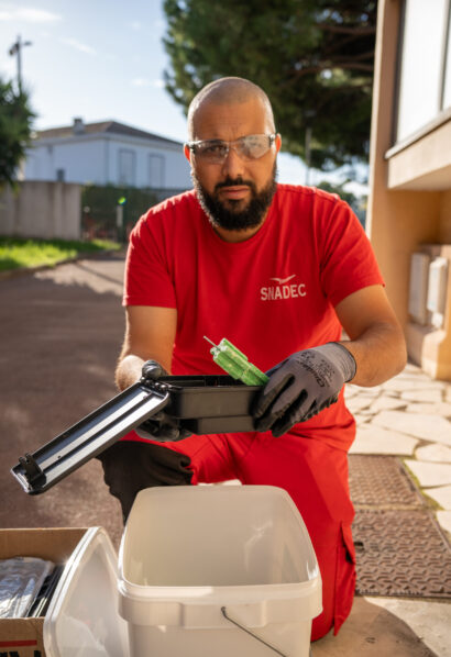 Technicien SNADEC en polo rouge intervenant au sol en extérieur, possiblement pour un traitement d'hygiène ou de surface.